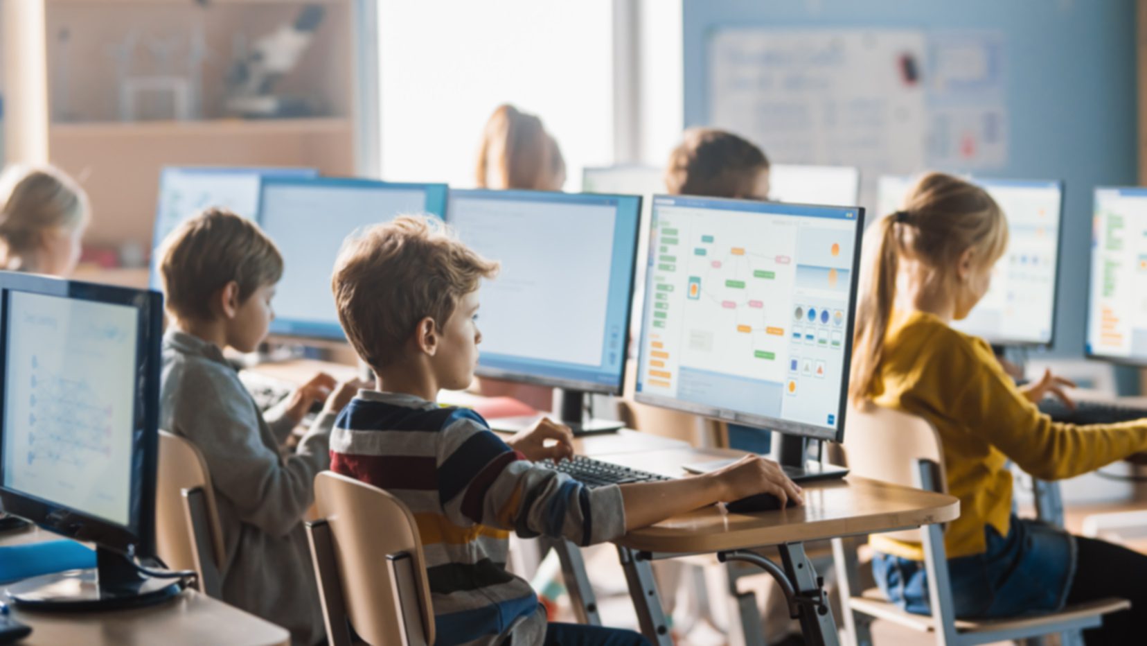 Kids working at desktop computers in a classroom, learning coding basics as part of a computer science for teachers program.
