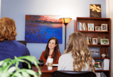 A small group of women sit around a desk in an office