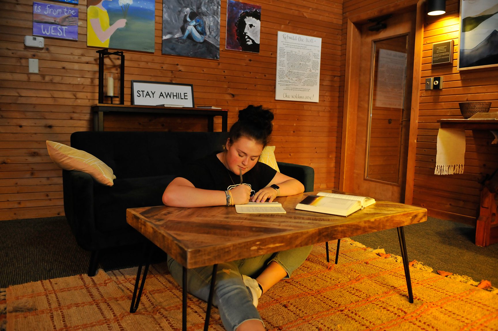 individualized studies student seated on floor, writing at low table